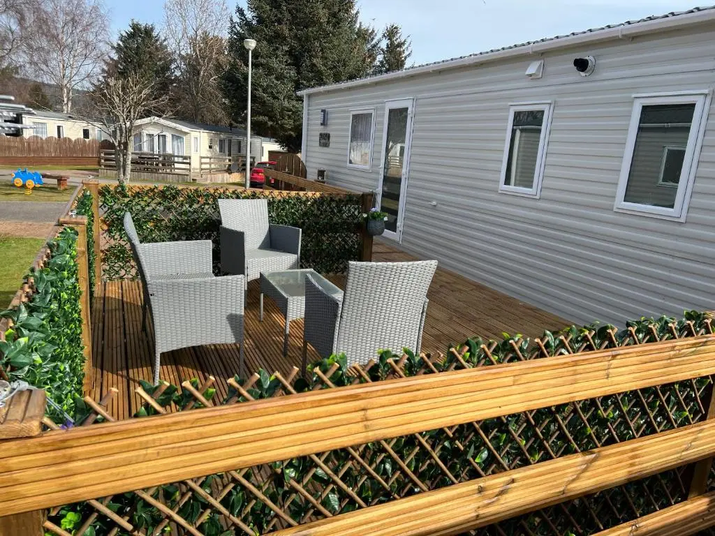 a wooden deck with white chairs and a house at The Highland Getaway 43 in Boat of Garten