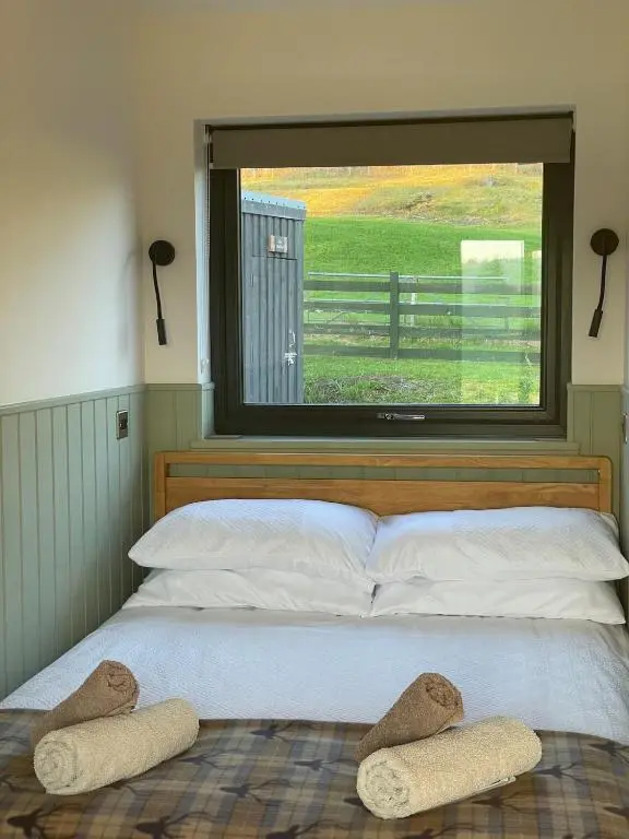 a bedroom with a bed with two large windows at The Wee Knoll in Invergarry
