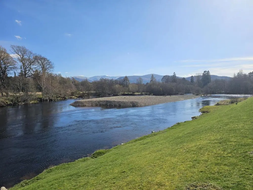 a river with a grassy field next to a river at Monash in Aviemore
