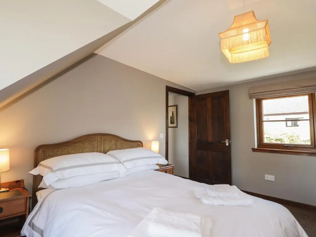 a bedroom with a bed with white sheets and a window at Fishers Cottage in Inverness