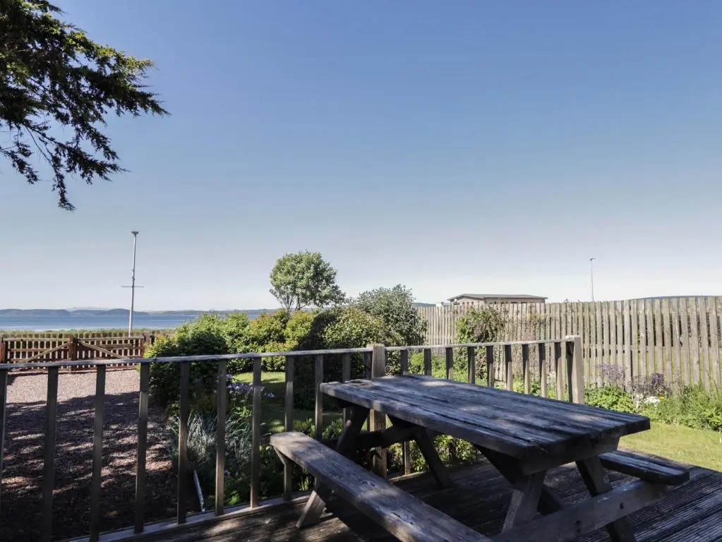 a wooden picnic table sitting next to a fence at Fishers Cottage in Inverness