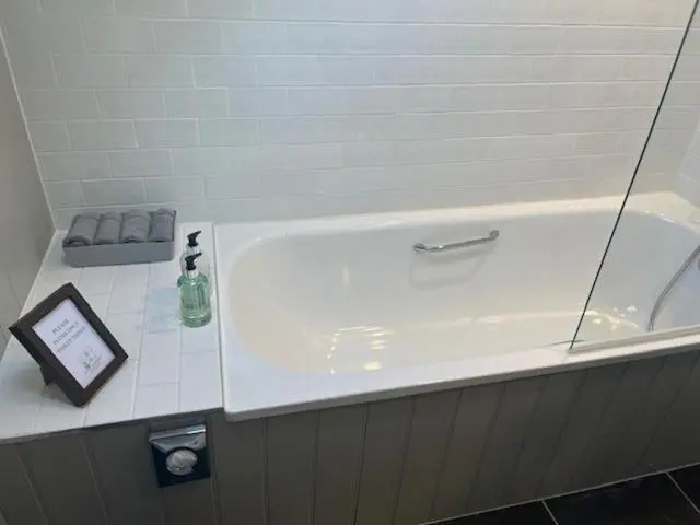 a white bath tub with a bottle on a counter at Balnain Street Cottage in Inverness