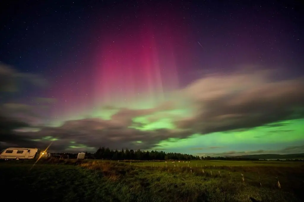 an aurora in the sky over a field at night at Woodend Caravan in Shinness