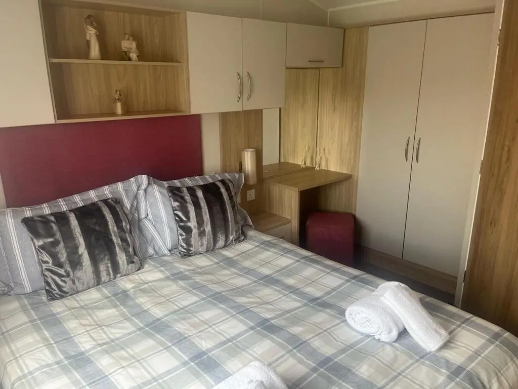 a bedroom with a bed with a plaid blanket and pillows at Woodend Caravan in Shinness