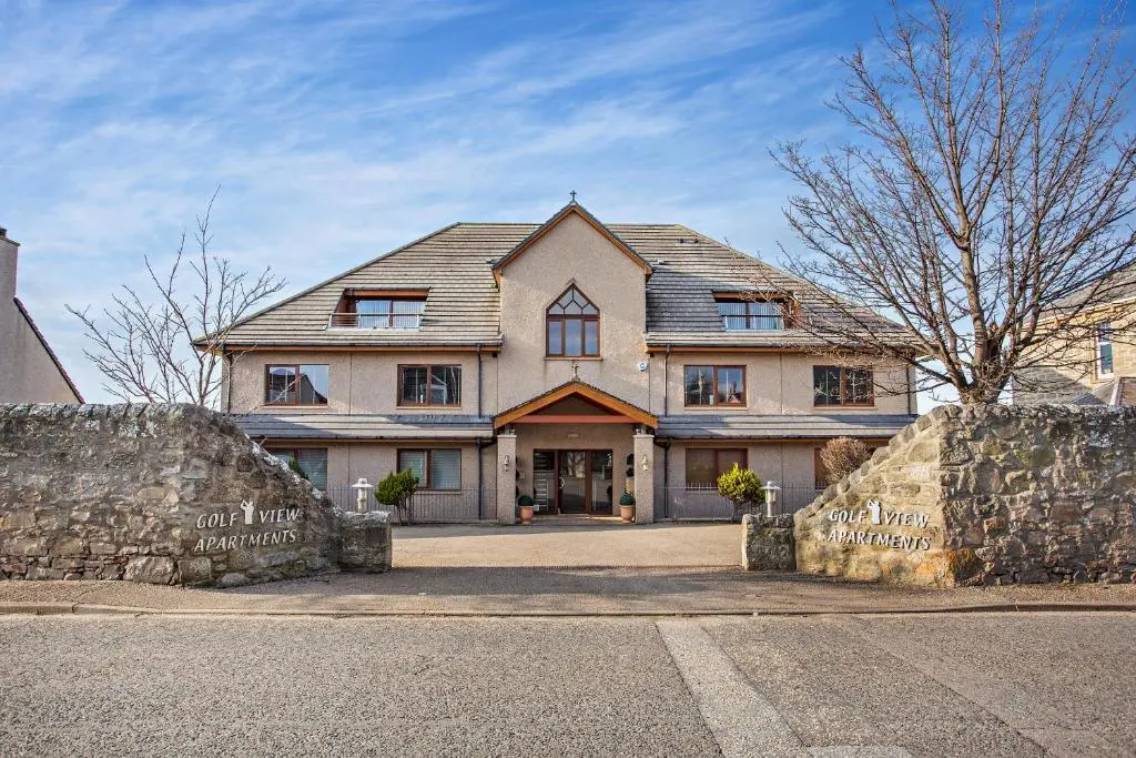 a large house with a stone wall in front of it at Penthouse Golf View Apartments in Lossiemouth