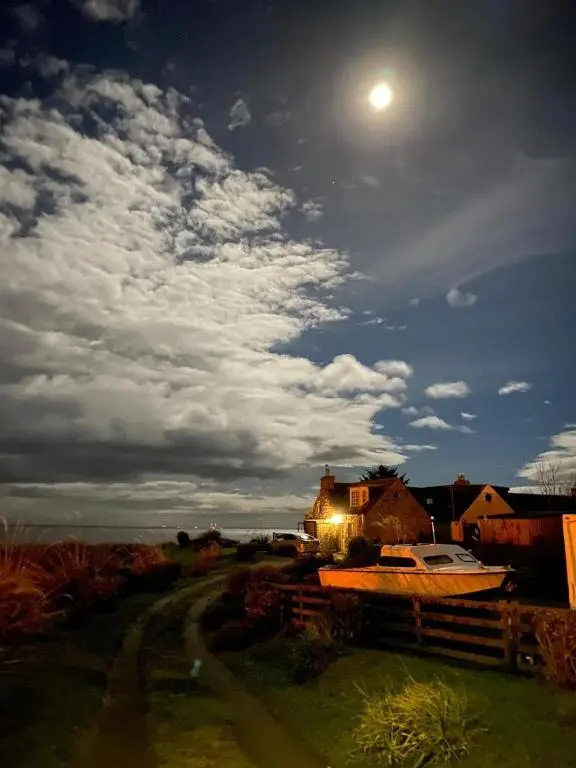 a house with a boat in a field at night at Cosy fisherman cottage in seaside village in Shandwick