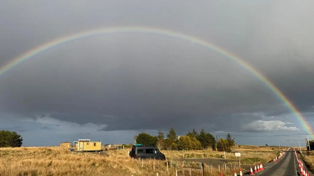 a rainbow in the sky over a road at The Cairn Hut in Lybster