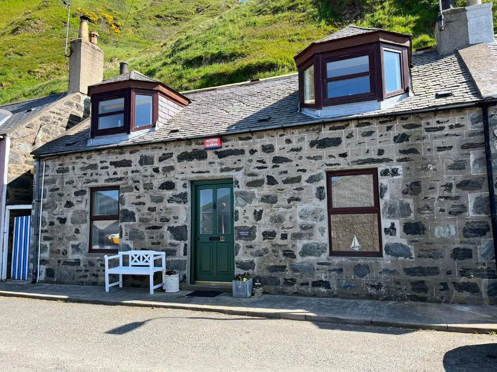 a stone building with a green door and windows at Lobster Pot in Banff