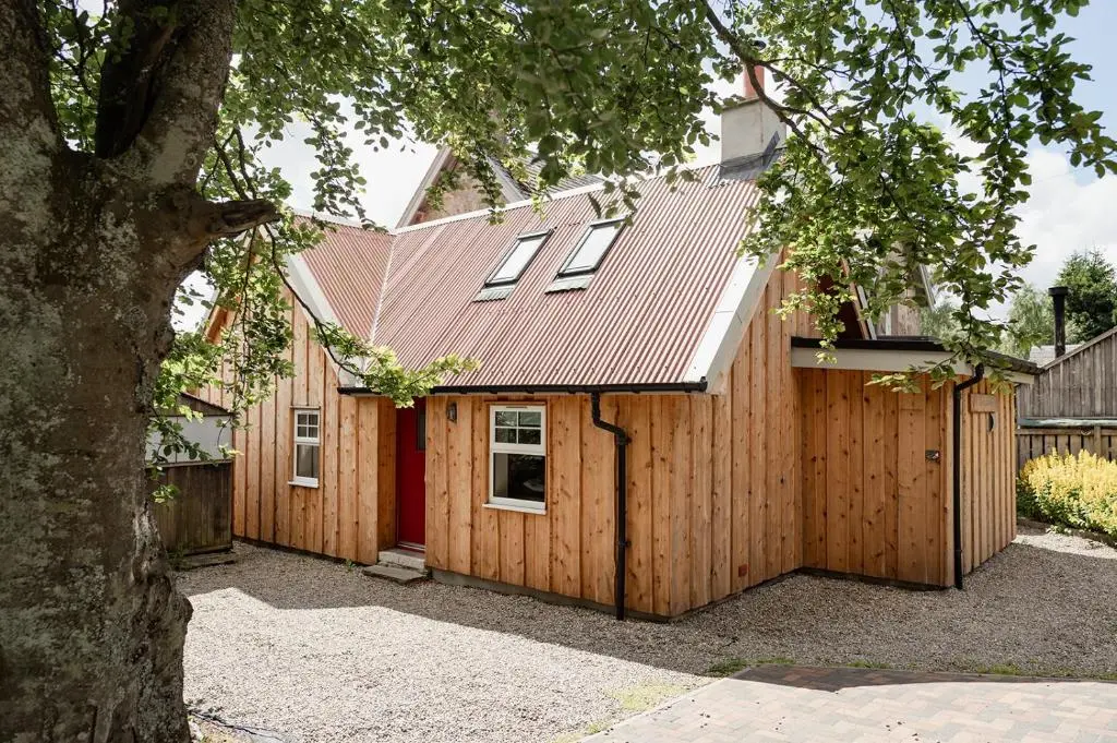 a house with a wooden fence and a red door at Broomfeild Bothy Comes with a Sauna in Boat of Garten