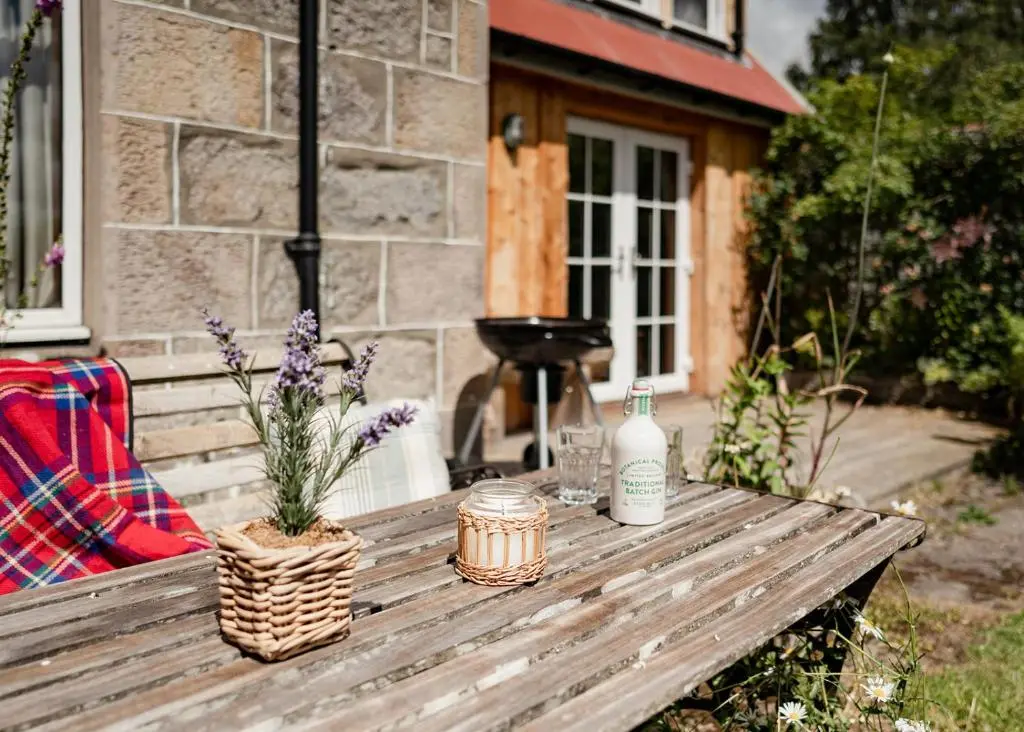 a wooden table with two bottles and flowers on it at Broomfeild Bothy Comes with a Sauna in Boat of Garten