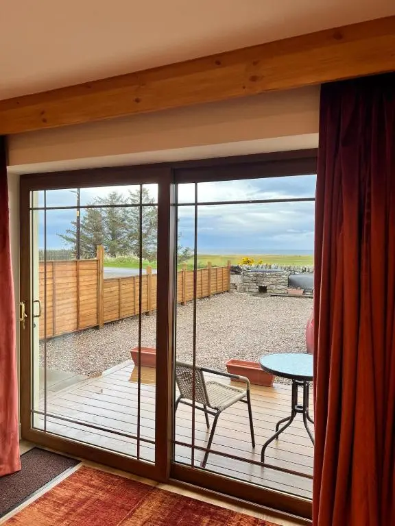 a sliding glass door leading to a patio with a table at Dalchalm Hideaway in Brora
