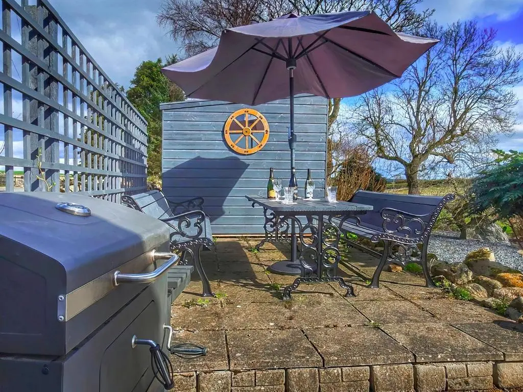 a patio with a table and an umbrella and a grill at Hogholm Farmhouse in Inverurie