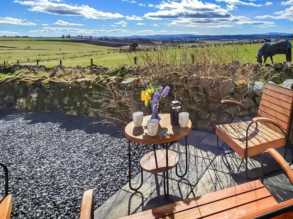 a table with flowers and cups and chairs on a patio at Hogholm Farmhouse in Inverurie