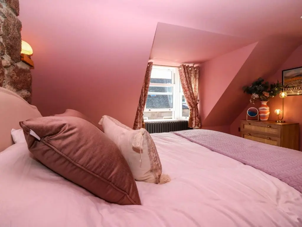 a bedroom with pink walls and a bed with pillows at Evansford in Ballater