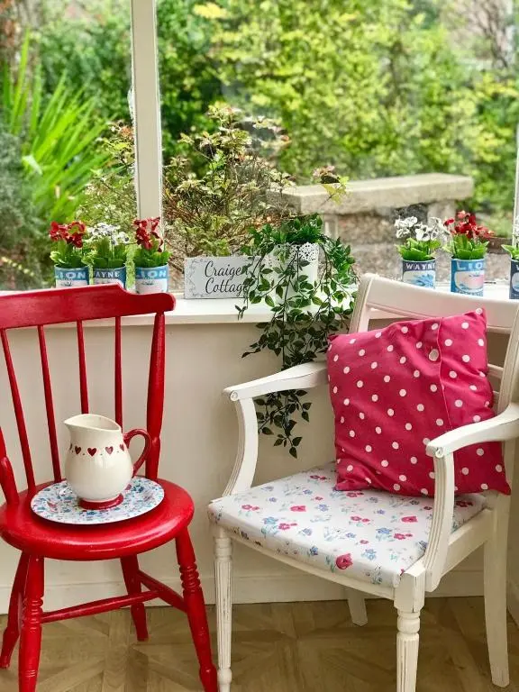 a red chair and a red chair with a tea pot on a window at Craigen Cottage Ballater in Ballater
