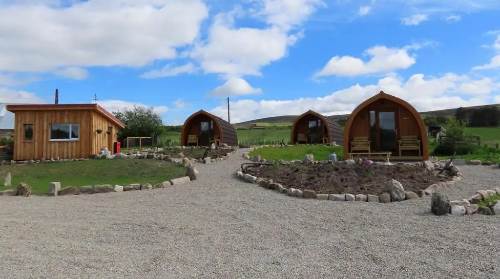 a group of small wooden huts in a field at Luxury Pod 3 in Bonar Bridge