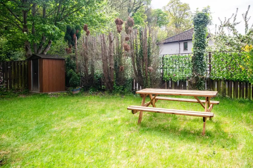 a wooden bench sitting in the grass near a fence at Highland Cow Apartment in Inverness