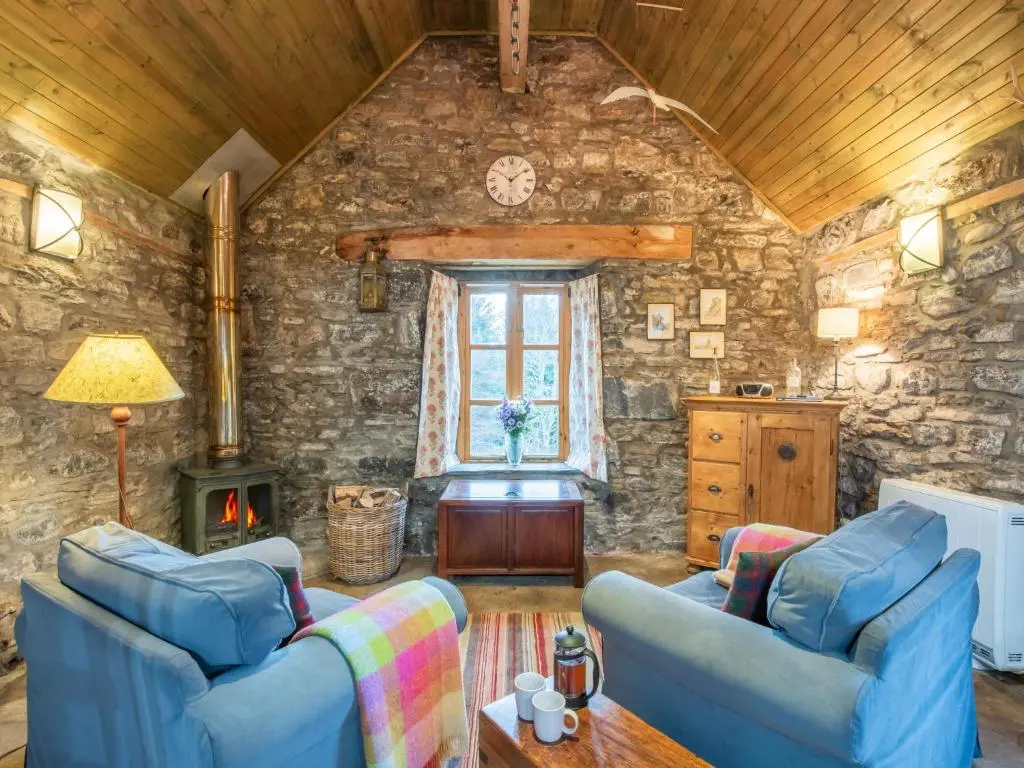 a living room with two blue couches and a stone wall at Holiday Home Farmburn Bothy by Interhome in Invermoriston