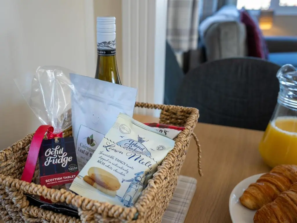 a basket with a bottle of wine and a plate of food at Chalet Lodge 3 by Interhome in Boat of Garten