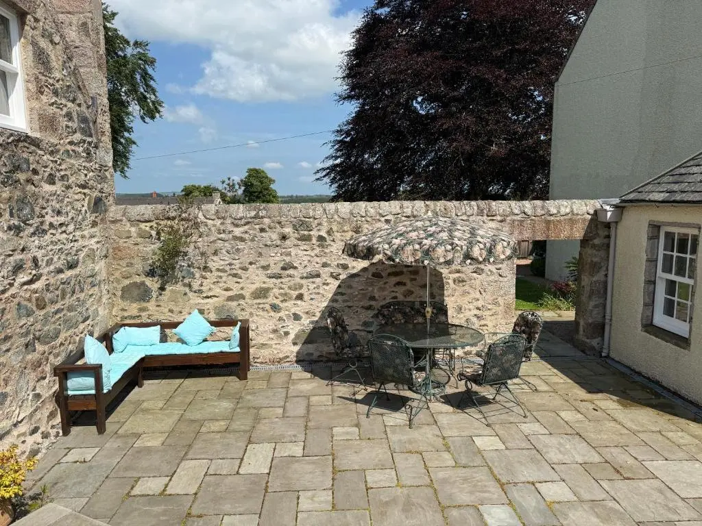 a patio with a table and a bench and a stone wall at The Old Manse Oyne in Oyne