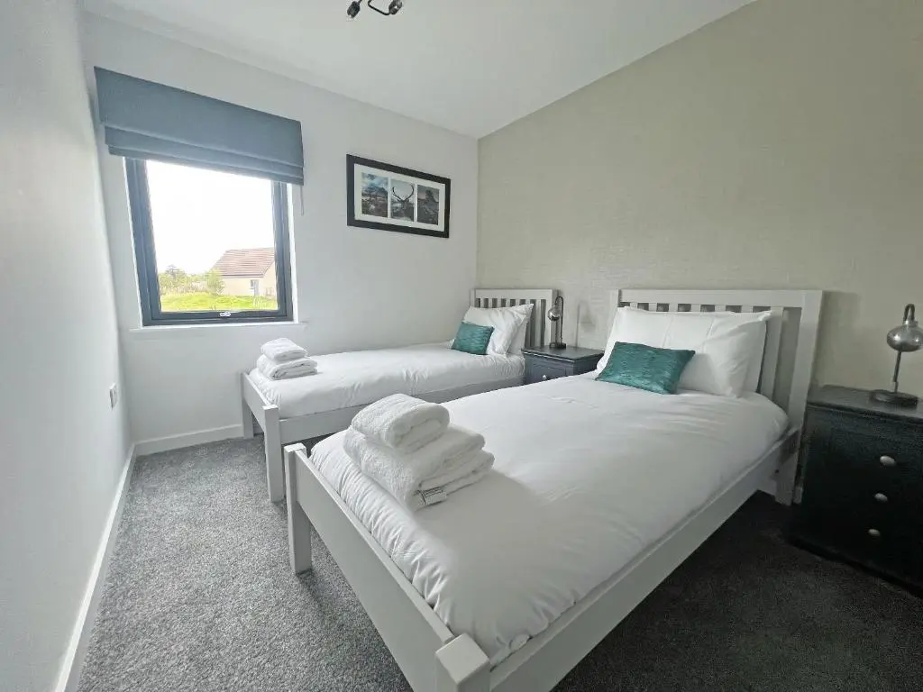 a white bedroom with two beds and a window at The Peaks in Aviemore