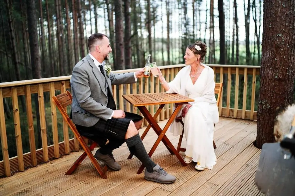 a man and a woman sitting at a table drinking wine at Treetops at Wildwoodz Off grid treehouse No electricity in Allangrange Station