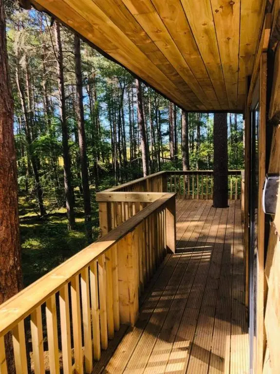 a wooden porch with a wooden roof in the woods at Treetops at Wildwoodz Off grid treehouse No electricity in Allangrange Station