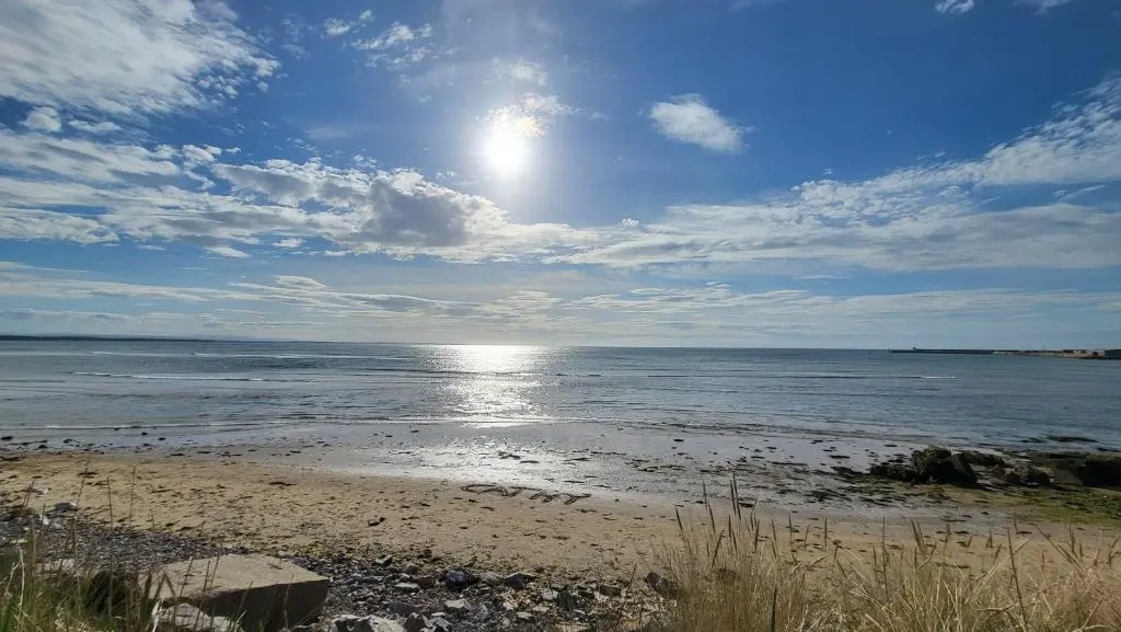 a beach with the sun shining on the water at Northern Light Villa, forest, beach and bubbles in Burghead