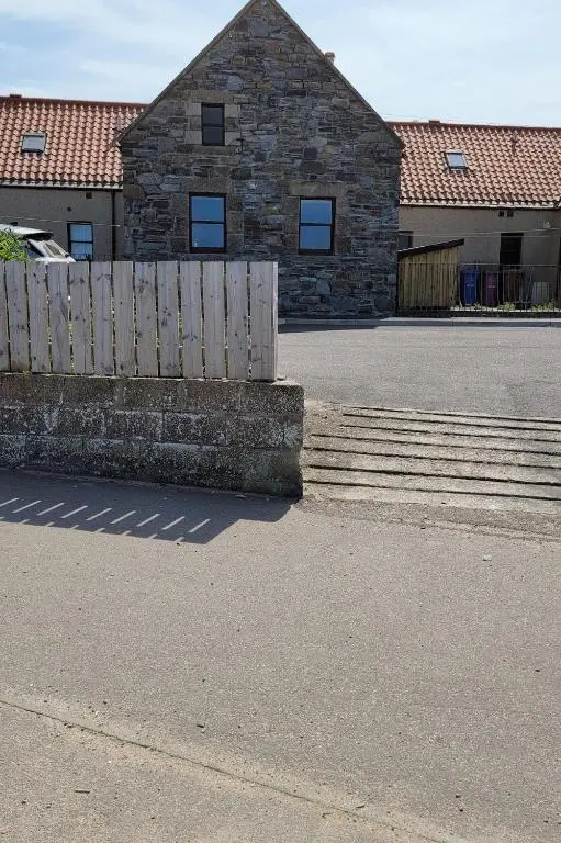 a building with a wooden fence in front of a street at Idyllic beach cottage 56 Seatown Cullen in Cullen