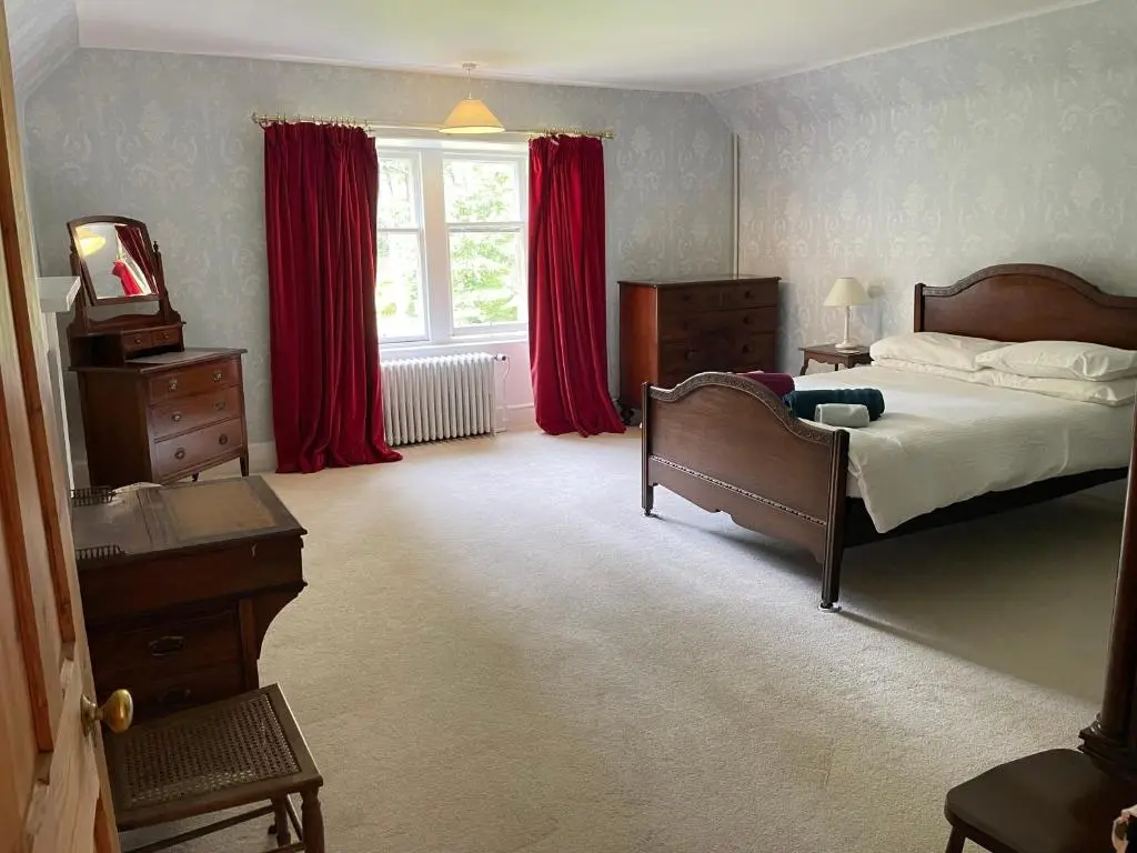 a bedroom with a bed and a window with red curtains at Glentromie Estate in Ruthven