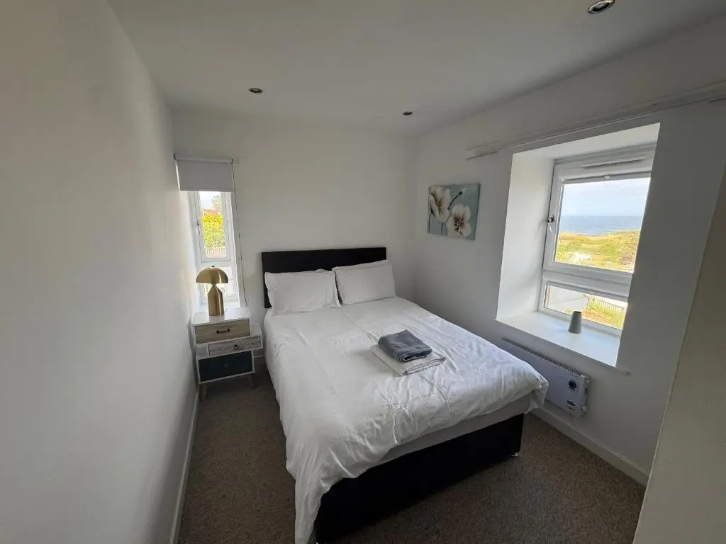 a small bedroom with a bed and two windows at Harbour View Hopeman in Hopeman