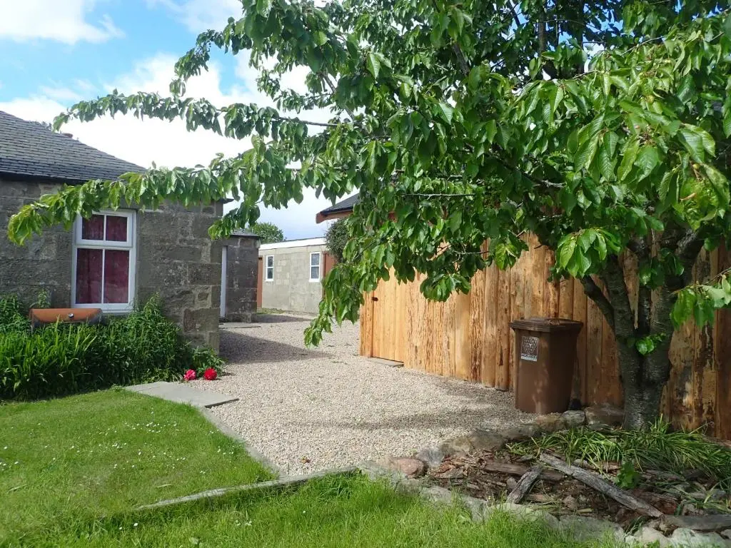 a fence and a tree next to a house at Private Speyside Tipi Retreat and Whisky Marrying Tun Hot Tub in Coltfield