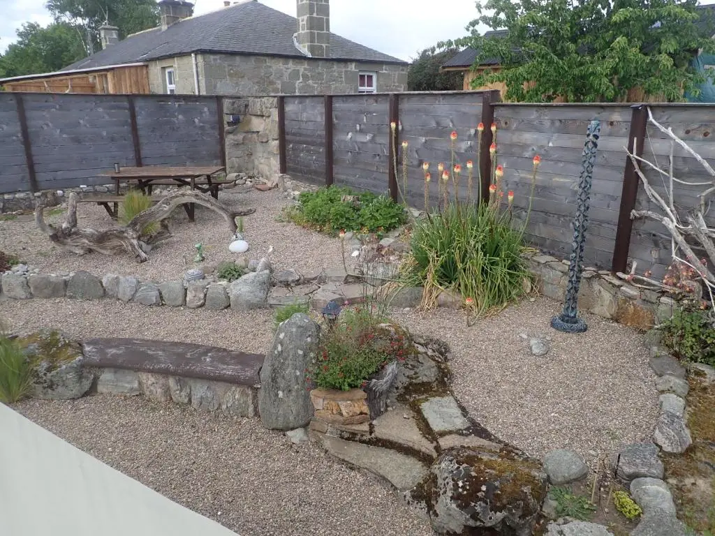 a garden with a fence and a bench and plants at Private Speyside Tipi Retreat and Whisky Marrying Tun Hot Tub in Coltfield