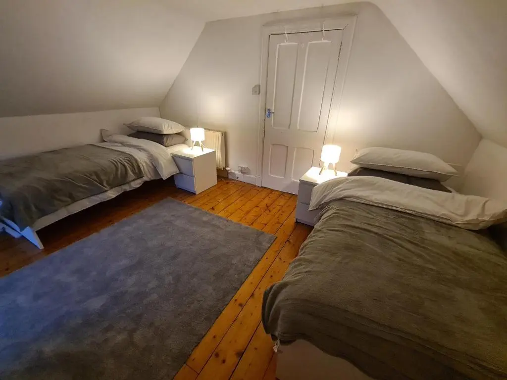 two beds in a room with two lamps and a rug at Alltachbeg in Tomintoul