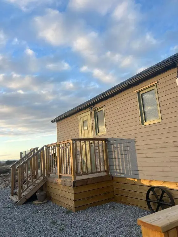 a house with a wooden deck with a staircase at Shephards Hut by the Beach in Findhorn
