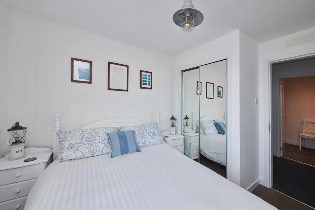 a white bedroom with a bed and a mirror at The Sandpiper in Burghead