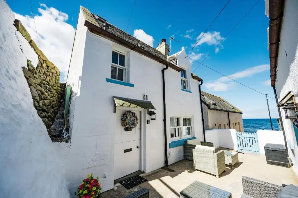 a white cottage with the ocean in the background at Nautical Nook, 16 Seatown, Gardenstown in Gardenstown