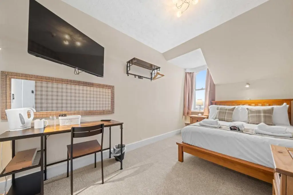 a bedroom with a bed with a desk and a tv at mySTAYINN Cedar Villa Guest House in Inverness