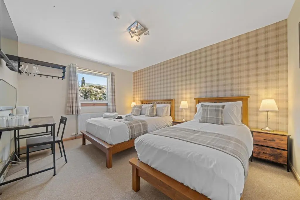 a bedroom with two beds and a desk and a window at mySTAYINN Cedar Villa Guest House in Inverness