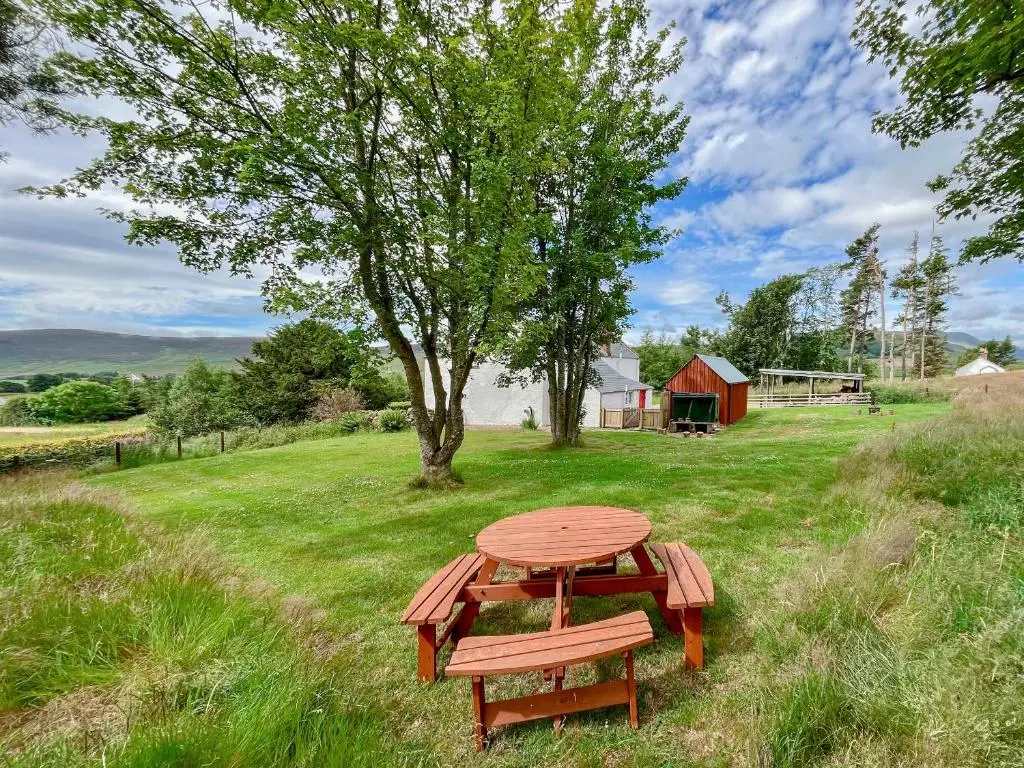 a picnic table in a field with a tree and a barn at Rottal Farmhouse in Millton of Clova