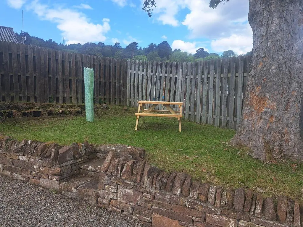 a wooden bench sitting in a yard next to a fence at Tweed Apartment, Golspie in Golspie