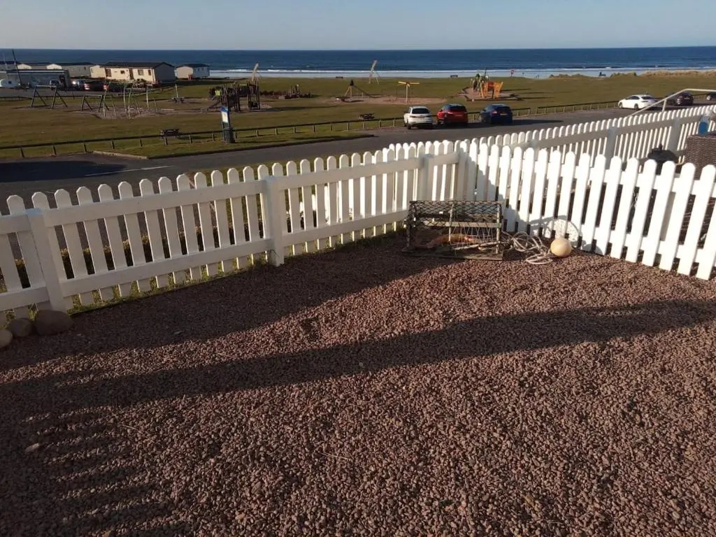 a white picket fence next to a beach and the ocean at Seabreeze in Whitehills