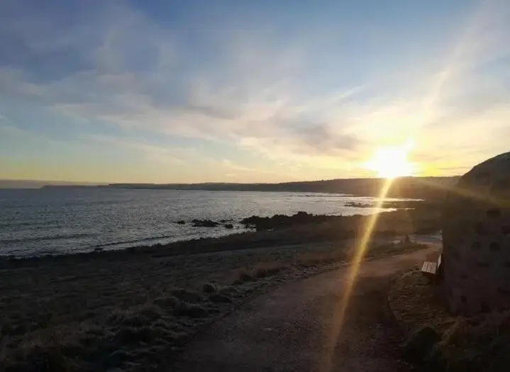 a sunset on a beach with the sun setting over the water at Seabreeze in Whitehills