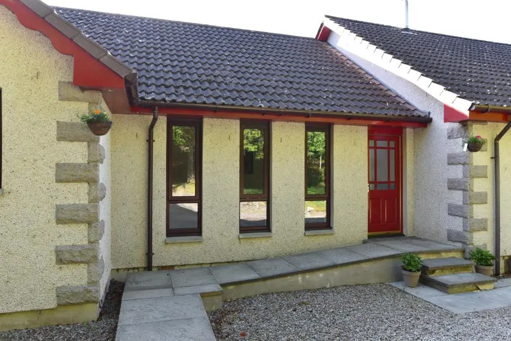 a small house with a red door and windows at Coille Burn in Urray