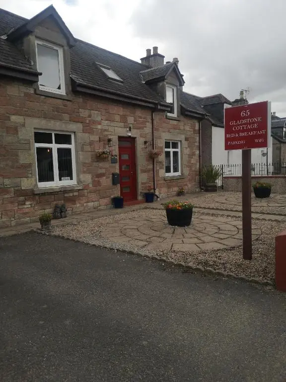 a sign in front of a brick house with a red door at Gladstone Cottage in Inverness
