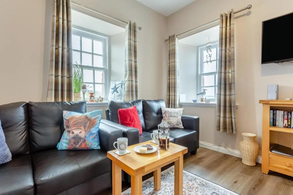 a living room with a black leather couch and a table at 2 Bed in Cromarty oc-s32047 in Cromarty