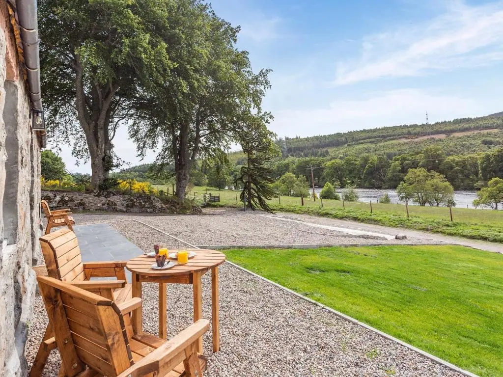 a patio with a table and chairs and a field at Ferry Cottage in Eskadale