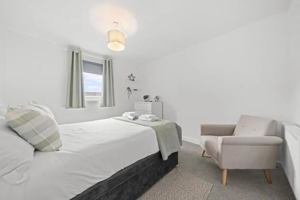 a white bedroom with a bed and a chair at Heather 3 Bedroom House - Inverness in Inverness