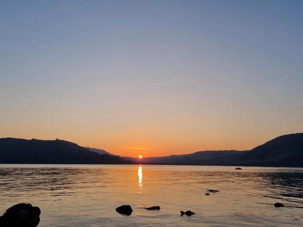 a sunset on a lake with rocks in the water at Bailem Lodge at Loch Ness ADULTS ONLY in Fort Augustus