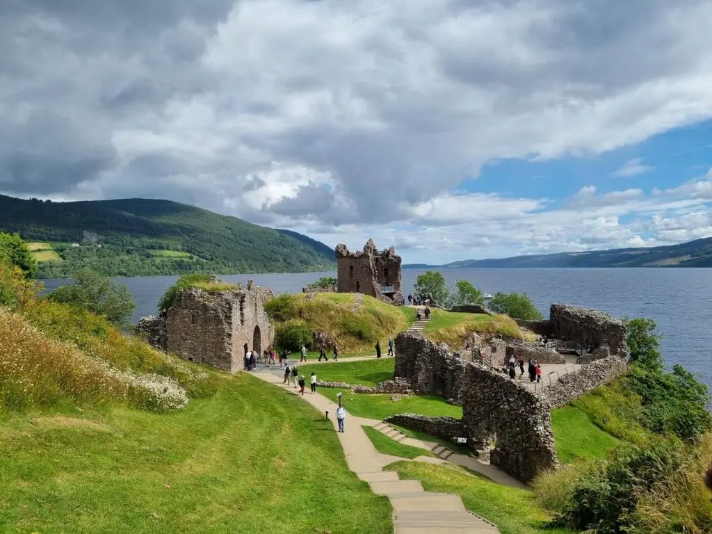 a castle on a hill next to a body of water at Bailem Lodge at Loch Ness ADULTS ONLY in Fort Augustus